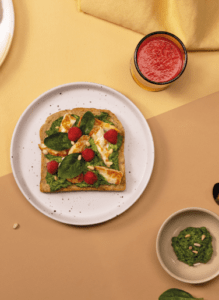 Photo d'une tranche de pain de mie maïs et graines dans une assiette. Dessus on y voit des épinards, des framboises et des morceaux de poulet.