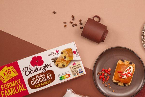 Une photo d'ambiance sur laquelle on voit un pack de pains au chocolat x16 La Boulangère ainsi qu'un Pain au chocolat avec des fraises et du muesli dans une assiette.