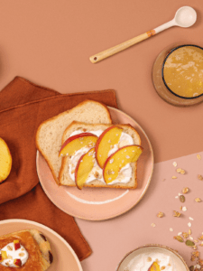 Photo de deux tranches de Brioche tranchée Bio dans une assiette. L'une est tartinée de fromage blanc et de 4 quartiers de pêche.